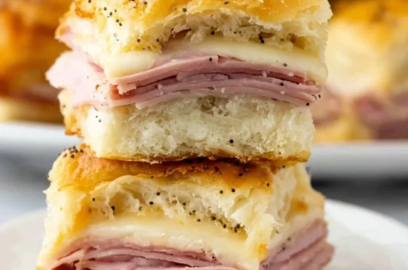 Baked ham and cheese sliders on a platter, topped with sesame seeds
